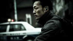 自転車で片耳イヤホンを装着しながら走行する日本人男性と背後を走る車の様子