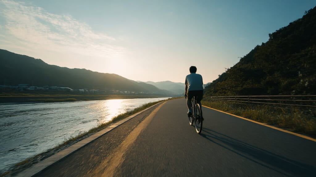 河川敷のサイクリングロードをクロスバイクで走る初心者の男性
