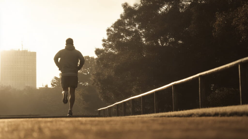 早朝の公園をランニングする日本人男性の健康的なトレーニング風景