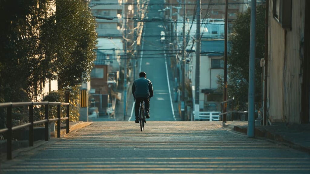 坂道で重さを感じながら自転車を押す日本人男性の様子